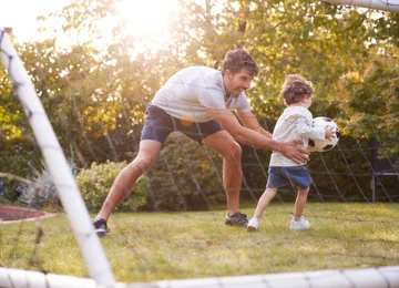 Far og søn spiller bold i haven. 