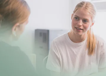 Ung med langt lyst hår taler med patient i lægeklinik i konsultation