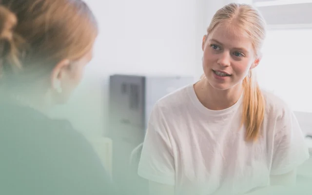 Ung med langt lyst hår taler med patient i lægeklinik i konsultation