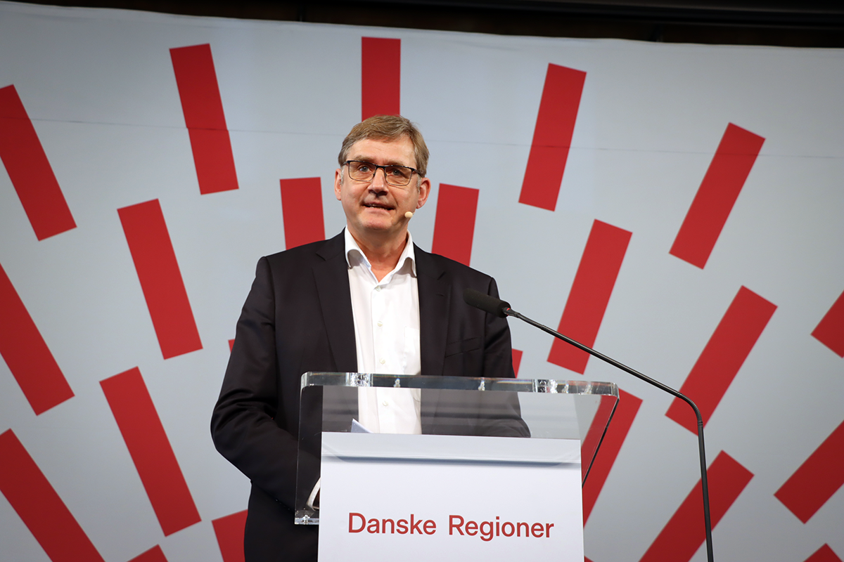 PLO's formand Jørgen Skadborg i jakkesæt ved talerstol, hvorpå der står Danske Regioner