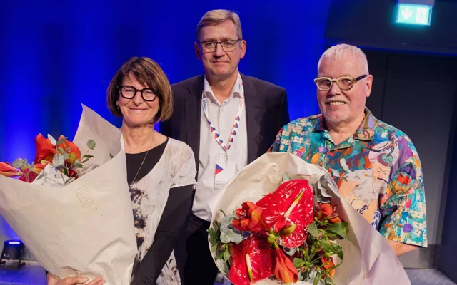 PLO's formand Jørgen Skadborg står imellem de to prisvindere, Berit Lassen og Helge Madsen. De har begge fået en buket blomster