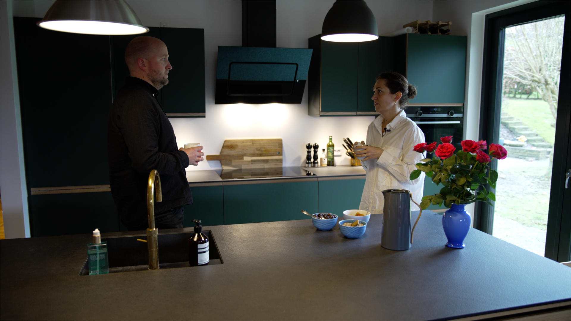 En mand og en kvinde står og taler sammen i et moderne køkken i et moderne hus. De står bag en køkken-ø.
