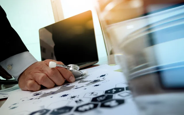 Hånd med stetoskop foran bord med diagram og tastatur