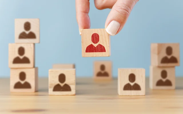 Hånd sætter træklods med rød figur ned blandt klodser med brune figurer