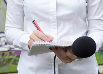 Journalist med notesbog og mikrofon i hånden