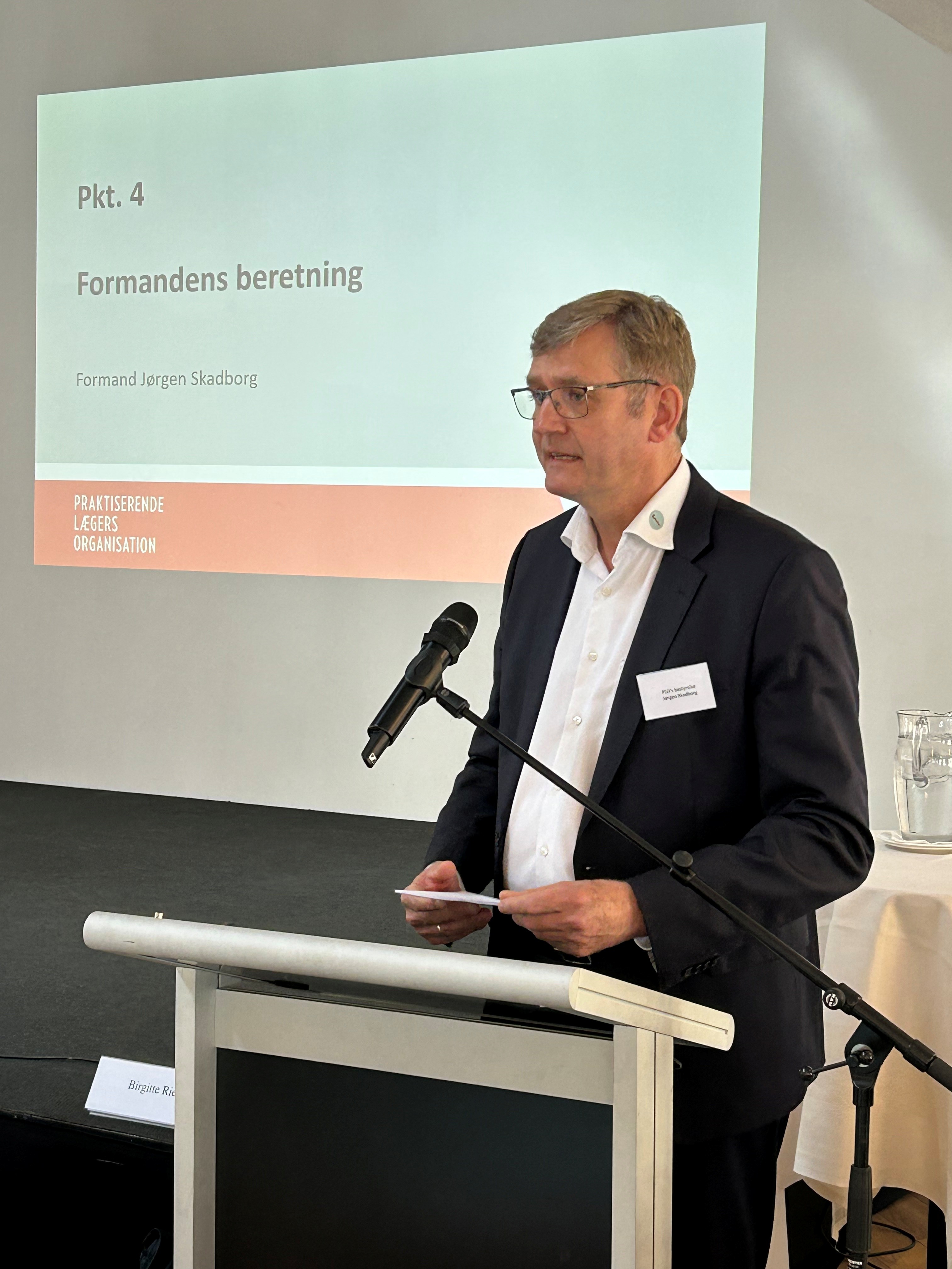 Jørgen Skadborg ved talerstol med præsentation i baggrunden