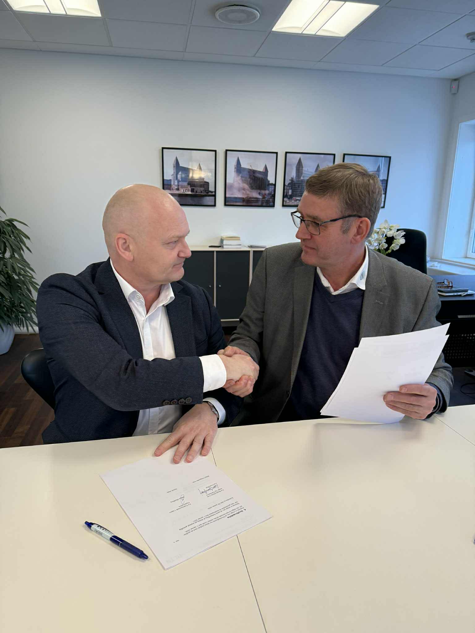 PLO's formand og RLTN's formand giver hånd til hinanden ved skrivebord med papirer (Aftale26).