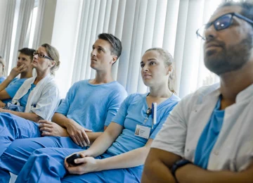 Læger på hospital sidder og lytter på et oplæg.