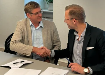 PLO's formand Jørgen Skadborg og formand for Danske Regioners Lønnings- og Takstnævn Heino Knudsen giver hinanden hånd efter at have indgået en ny overenskomst for de praktiserende læger. De er begge iført jakkesæt og har briller på