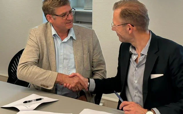 PLO's formand Jørgen Skadborg og formand for Danske Regioners Lønnings- og Takstnævn Heino Knudsen giver hinanden hånd efter at have indgået en ny overenskomst for de praktiserende læger. De er begge iført jakkesæt og har briller på
